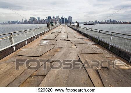 Stock Image - Jetty reaching out into the Hudson river, Liberty Island. Manahttan skyline in background. New York. USA.. Fotosearch