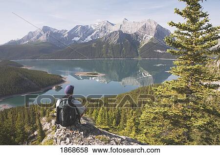 Kananaskis Country, Alberta, Canada; A Male Hiker Sitting On A Rock Ledge Overlooking Upper Kananaskis Lake View Large Photo Image Stock Photo - Kananaskis Country, Alberta, Canada; A Male Hiker Sitting On A Rock Ledge Overlooking Upper Kananaskis Lake. Fotosearch