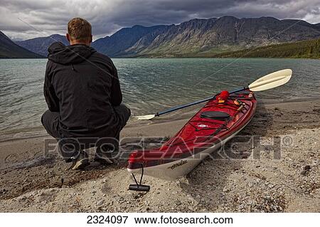Kayaker squatting by his kayak on the shoreline of Kusawa Lake; Yukon, Canada View Large Photo Image Stock Photo - Kayaker squatting by his kayak on the shoreline of Kusawa Lake; Yukon, Canada. Fotosearch