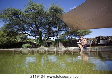 Kenya, Guest relaxing reading book beside swimming pool at luxurious Joy's Camp; Shaba National Reserve View Large Photo Image Picture - Kenya, Guest relaxing reading book beside swimming pool at luxurious Joy's Camp; Shaba National Reserve. Fotosearch