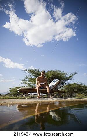 Stock Photo - Kenya, Guest relaxing reading book beside swimming pool at luxurious Joy's Camp; Shaba National Reserve. Fotosearch