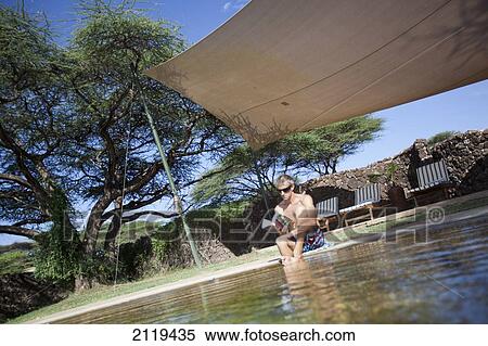 Stock Photography - Kenya, Guest relaxing reading book beside swimming pool at luxurious Joy's Camp; Shaba National Reserve. Fotosearch