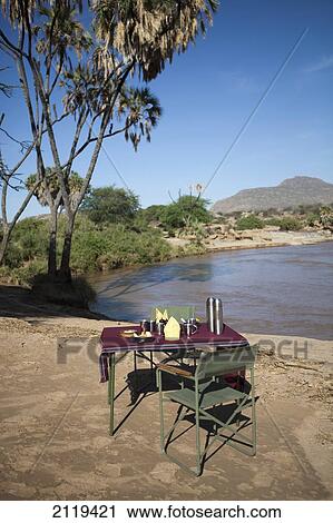 Stock Image - Kenya, Riverside breakfast table set up for guests at Joy's Camp; Shaba National Reserve. Fotosearch