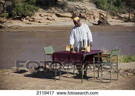 Stock Photo - Kenya, Riverside breakfast table set up for guests at Joy's Camp; Shaba National Reserve. Fotosearch