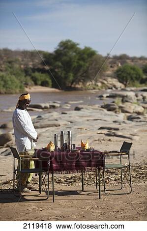 Stock Photo - Kenya, Riverside breakfast table set up for guests at Joy's Camp; Shaba National Reserve. Fotosearch