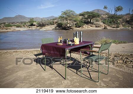 Stock Photo - Kenya, Riverside breakfast table set up for guests at Joy's Camp; Shaba National Reserve. Fotosearch