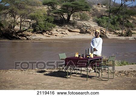 Stock Photograph - Kenya, Riverside breakfast table set up for guests at Joy's Camp; Shaba National Reserve. Fotosearch