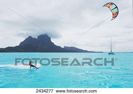 Stock Photo - Kiteboarding in the lagoon over tropical blue water; Bora Bora, French Polynesia. Fotosearch