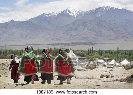 Stock Photo - Ladakhi Women In Traditional Dress And Hats Walking Under Snowcapped Mountains. Fotosearch