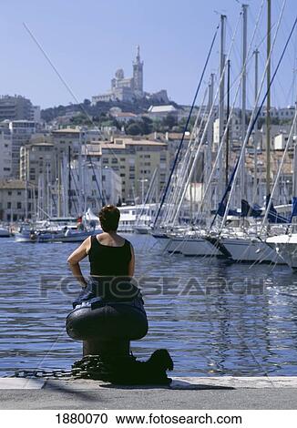 Stock Image - Lady Sitting Beside The Harbor With Her Dog With Notre Dame De La Garde Cathedral On The Hill Behind. Fotosearch