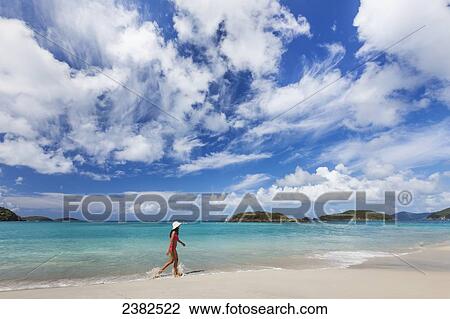 Stock Image - Lady walks along the tropical beach in the Virgin Islands; United States of America. Fotosearch