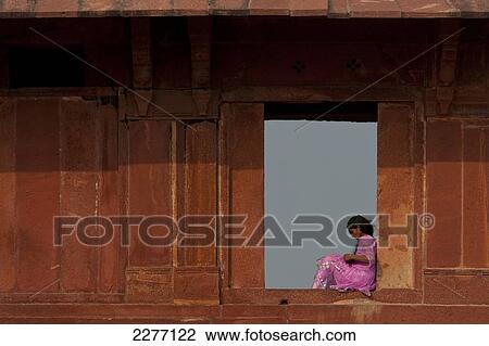 Stock Image - Lady wearing sari sitting in open window of building in Fatehpur Sikri, Agra, India.. Fotosearch