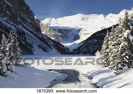 Stock Image - Lake Louise, Alberta, Canada; Mount Victoria In Winter With Snow Covered Trees And Open Water In A Creek. Fotosearch