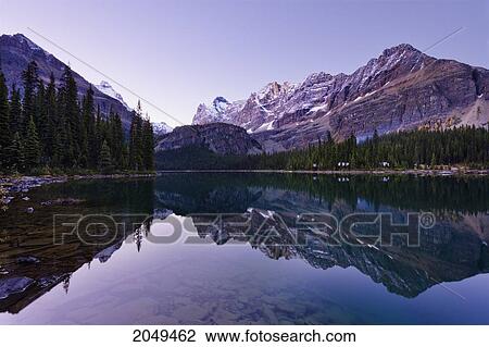 Stock Image - Lake O'hara, Log Cabins And Reflection Of Schaffer Ridge At Dawn, Yoho National Park, British Columbia. Fotosearch