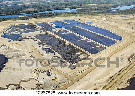 Stock Photography - landscape aerial view shows various stages of tailings ponds collecting oil sands productiion waste out in the open next to the Athabasca River; Fort McMurray, Alberta, Canada. Fotosearch