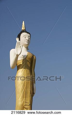 Stock Photo - Laos, Vientiane, Wat That Luang Neua, Buddha statue against blue sky.. Fotosearch