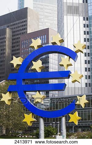 Stock Image - Large Euro monument against the background of large skyscrapers; Frankfurt am Main, Germany. Fotosearch