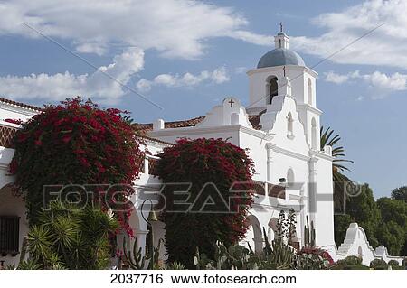 Stock Photograph - Large Flowering Shurbs In Front Of White Church With Steeple And Blue Sky And Clouds; Oceanside California United States Of America. Fotosearch