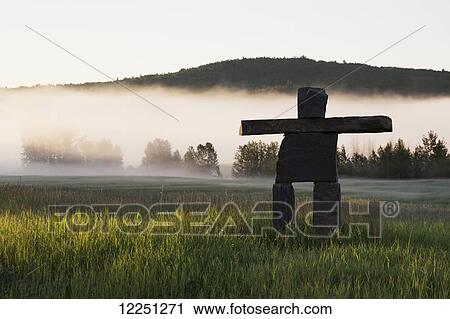 Large rock Inuit inukshuk in grassy field with morning fog in the distance and trees with rolling hills; Alberta, Canada View Large Photo Image Stock Image - Large rock Inuit inukshuk in grassy field with morning fog in the distance and trees with rolling hills; Alberta, Canada. Fotosearch