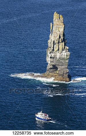 Stock Photography - Large sea stack rock structure in the ocean with tour boat; Liscannor, County Clare, Ireland. Fotosearch