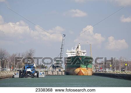 Stock Photo - Large Ship In Welland Canal, Bridge Raised With Clouds And Blue Sky; Port Colborne, Ontario, Canada. Fotosearch