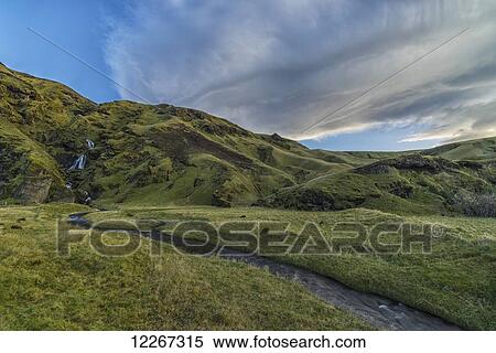 Stock Photography - Lenticular clouds form over a waterfall and stream running towards the ocean near Vik; Iceland. Fotosearch