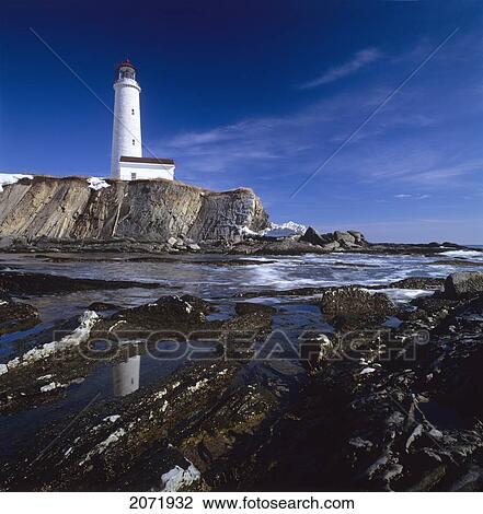 Stock Image - Lighthouse By A Rocky Shore, Cap-Des-Rosiers, Gaspe Coast, Quebec. Fotosearch