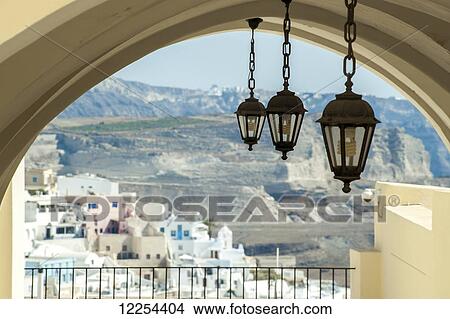 Picture - Lights hang from an arched ceiling with a view of a church, whitewashed buildings and landscape; Fira, Santorini, Greece. Fotosearch