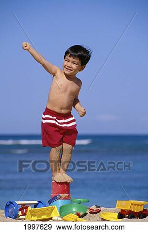 Stock Photo - Little Boy Stands On Bucket, Smiling With Arm Up, Surrounded With Beach Toys. Fotosearch