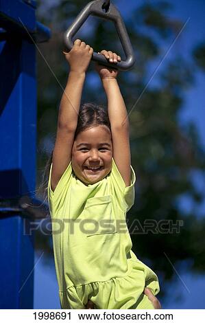 Stock Image - Little Girl Smiling Hanging On Jungle Gym, Blue Sky Background B1088. Fotosearch