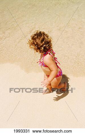 Stock Image - Little Girl With Blond Curly Hair Plays On The Beach. Fotosearch