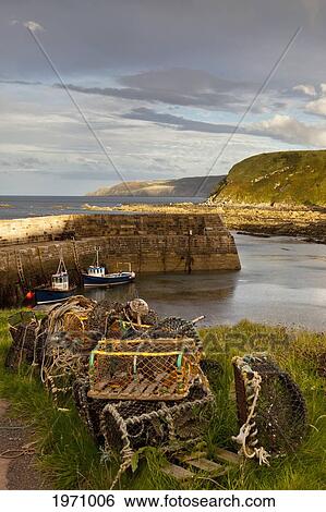 Stock Photograph - Lobster Traps On The Shore And Boats Mooring In The Water; Cove Lothian Scotland. Fotosearch