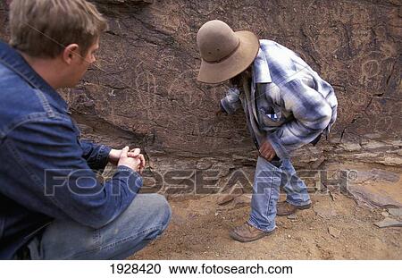 Stock Image - Local Guide Showing Tourist Aboriginal Rock Carvings. Fotosearch