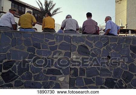 Stock Image - Local Men Sitting On Stone Wall. Fotosearch