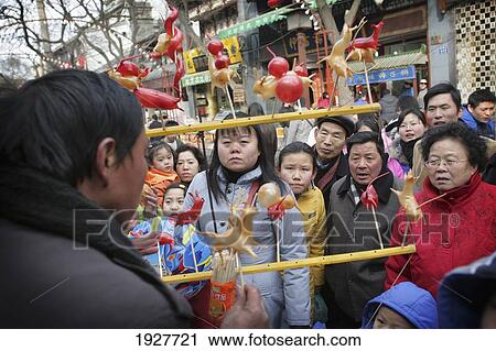 Stock Image - Locals Watch A Chinese Street Seller Making Plastic Animals, Xi'an, Capital Of Shaanxi Province, China. Fotosearch
