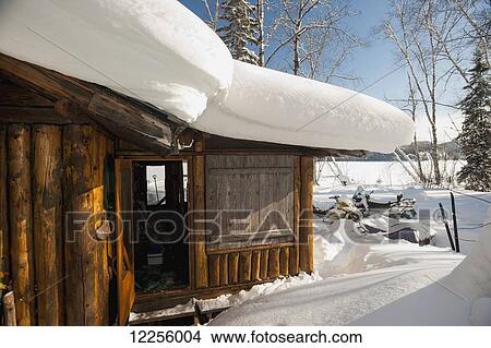 Picture - Log cabin covered in snow in winter near a frozen lake; Ontario, Canada. Fotosearch