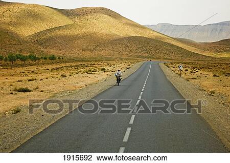 Stock Image - Lone Cyclist Along Desert Road. Fotosearch
