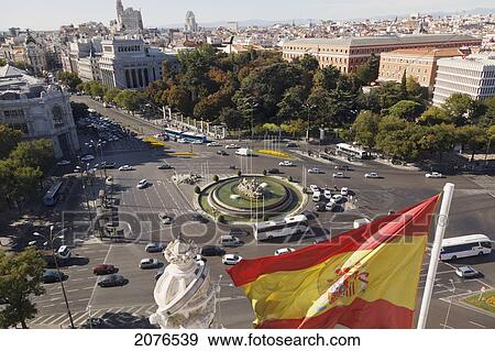 Stock Photo - Looking Across Plaza De La Cibeles And Up Calle De Alcala With A Spanish Flag In The Foreground; Madrid Spain. Fotosearch
