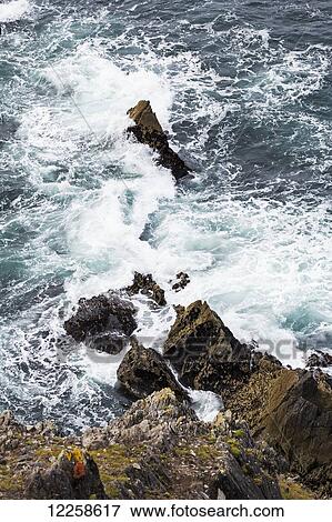 Stock Photo - Looking down on a rocky cliff with waves crashing on rocks; Dingle, County Kerry, Ireland. Fotosearch