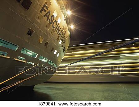 Stock Image - Looking Past Tied Up Cruise Ship To Another Cruise Ship Leaving Nassau Harbor, Blurred Motion. Fotosearch