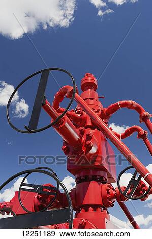 Stock Photo - Low angle close up of red oil well head (Christmas Tree) with blue sky and clouds; Calgary, Alberta, Canada. Fotosearch