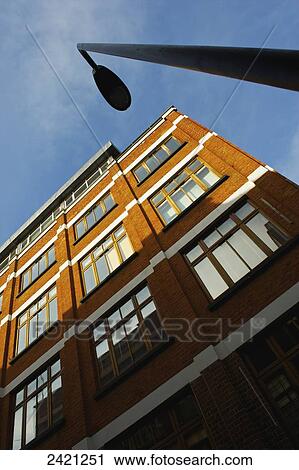 Stock Image - Low angle view of a brown brick building, street light and blue sky, Shoreditch; London, England. Fotosearch