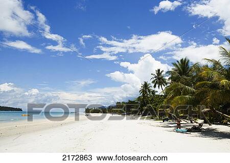 Stock Image - Malaysia, Pantai Cenang (Cenang beach); Pulau Langkawi, blue skies and islands in background, White sandy beach with palm trees. Fotosearch