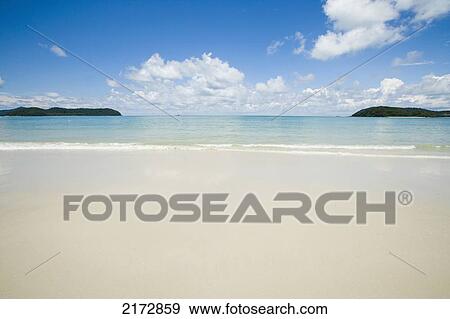 Stock Photo - Malaysia, Pantai Cenang (Cenang beach); Pulau Langkawi, islands in background, Wide open view of white sandy beach and blue sky. Fotosearch