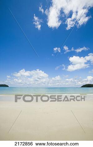 Stock Photograph - Malaysia, Pantai Cenang (Cenang beach); Pulau Langkawi, islands in background, Wide open view of white sandy beach and blue sky. Fotosearch