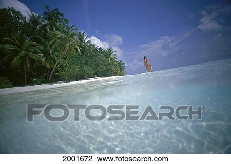 Stock Image - Maldives, Woman With Snorkel Gear Walks Along Shoreline Distance, Calm Clear Ocean. Fotosearch