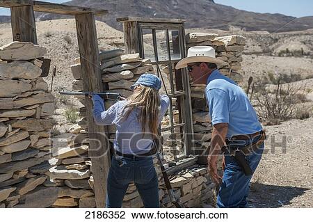 Stock Image - Male Instructor Guides Young Woman About How To Fire Shotgun At Lajitas Resort, Big Bend National Park And Big Bend State Park, South West Texas, Usa. Fotosearch