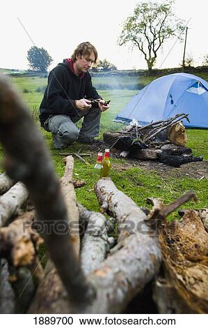 Stock Image - Male Preparing A Open Log Fire While Camping. Fotosearch
