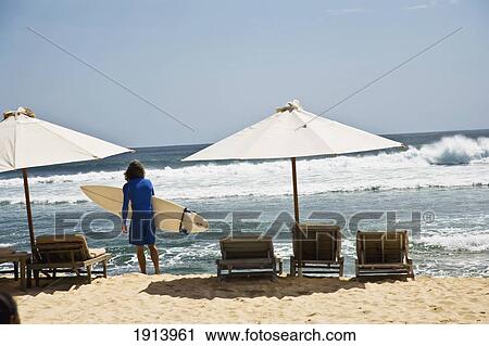 Stock Image - Male Surfer Standing On Beach. Fotosearch