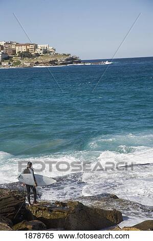 Stock Photography - Male Surfer Standing On Rocks At Bondi Beach. Fotosearch